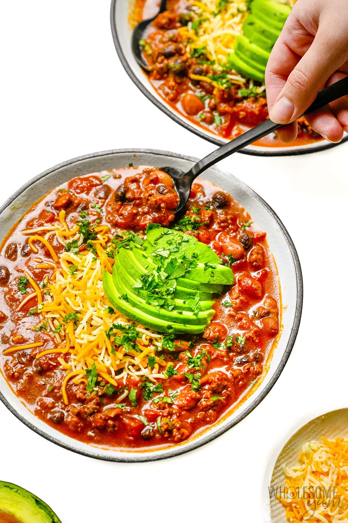 Bowl of chili with cheese, avocado and sour cream on top. 