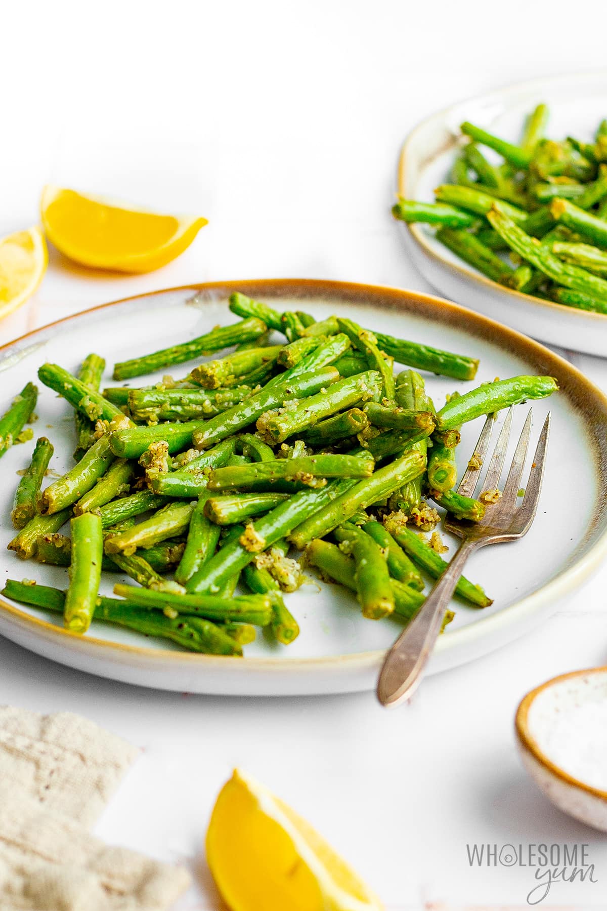 Air fryer green beans on plates with lemon wedges and a fork.