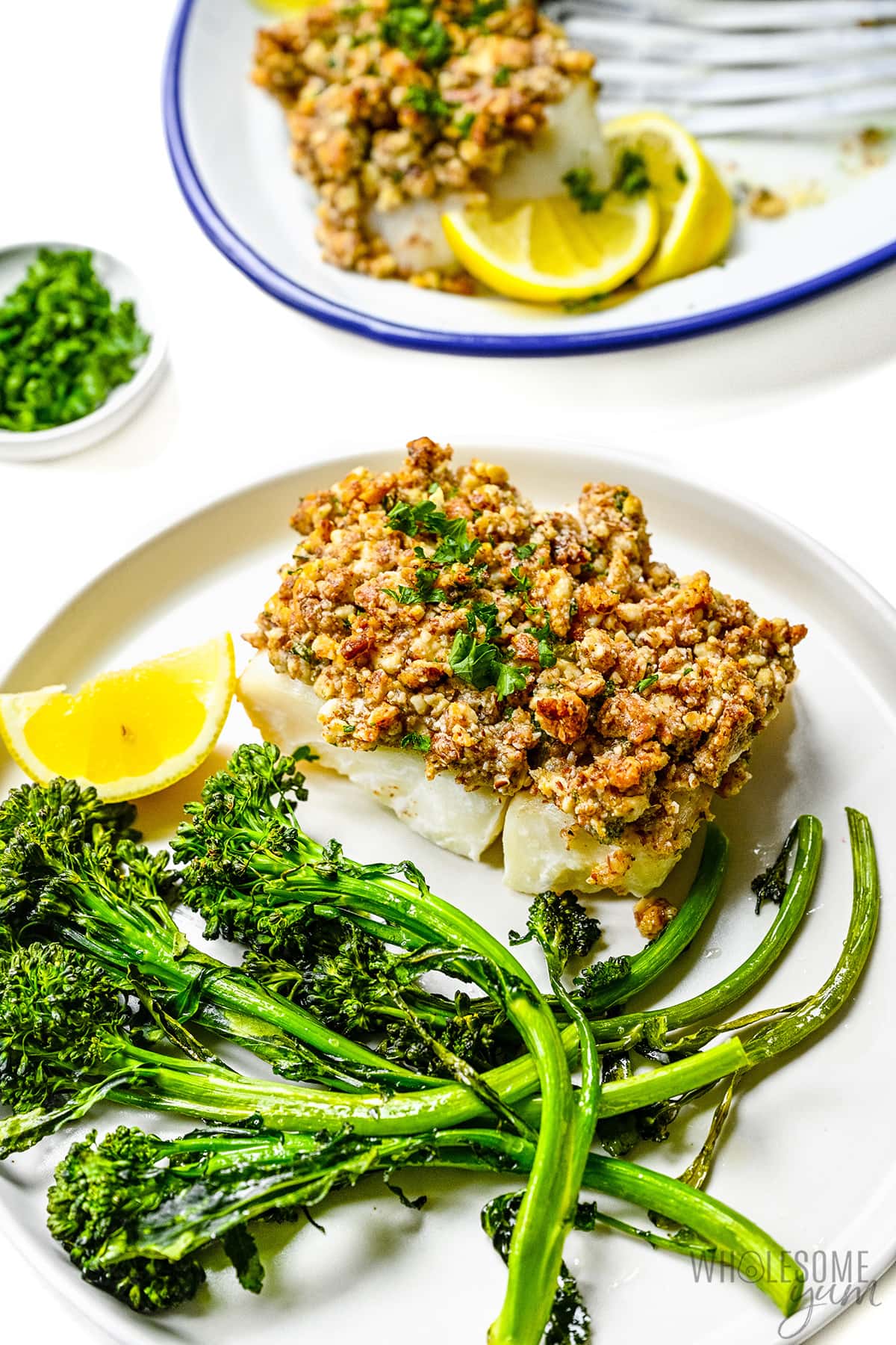 Baked haddock on a plate with broccolini and lemon slices.