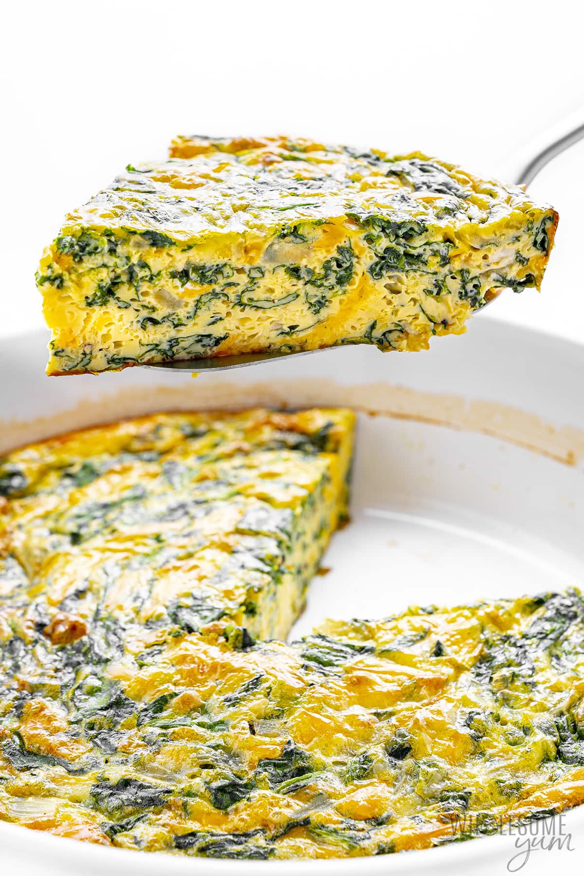 Slice of spinach quiche removed from baking dish.