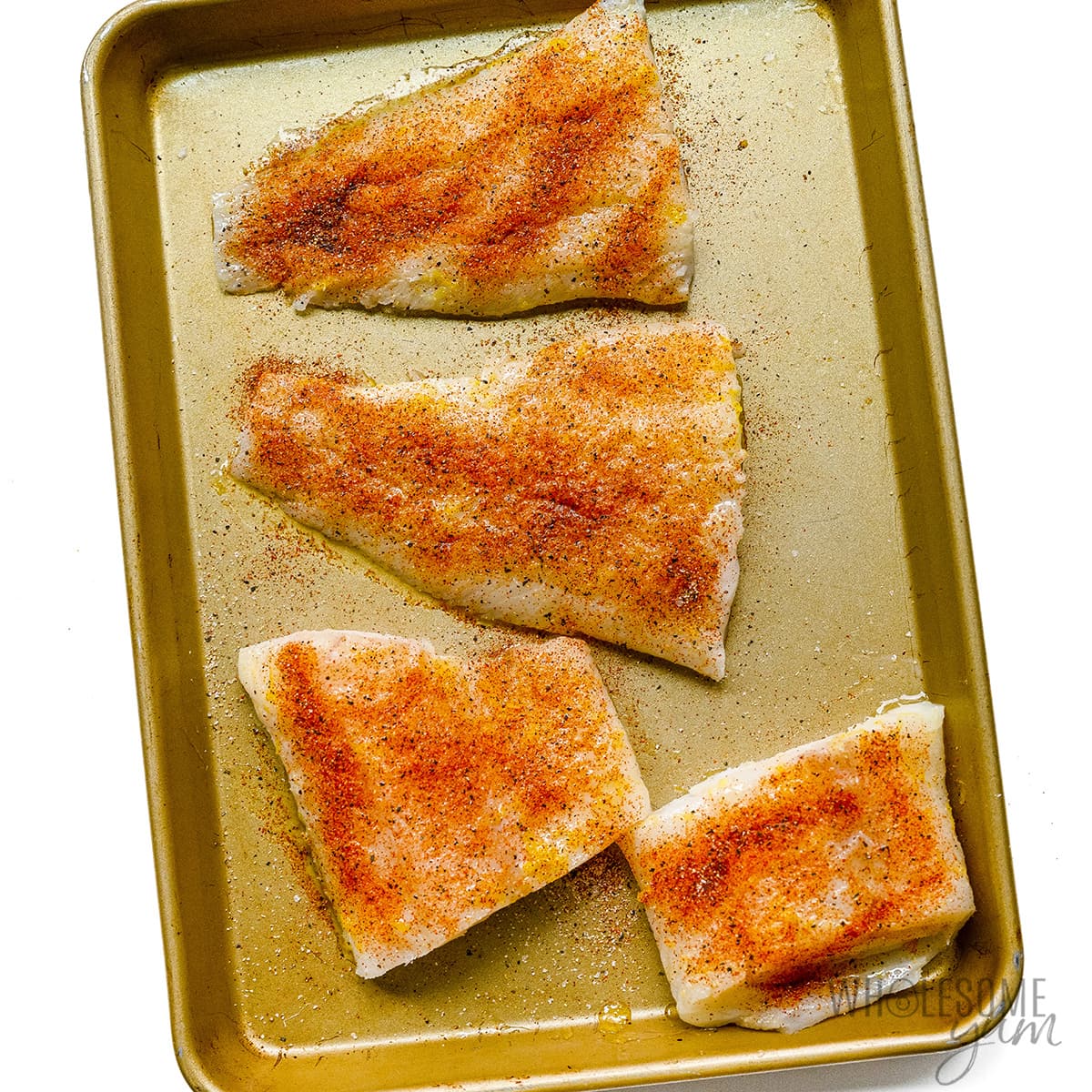 Cod fillets brushed with oil and spices on  a sheet pan.