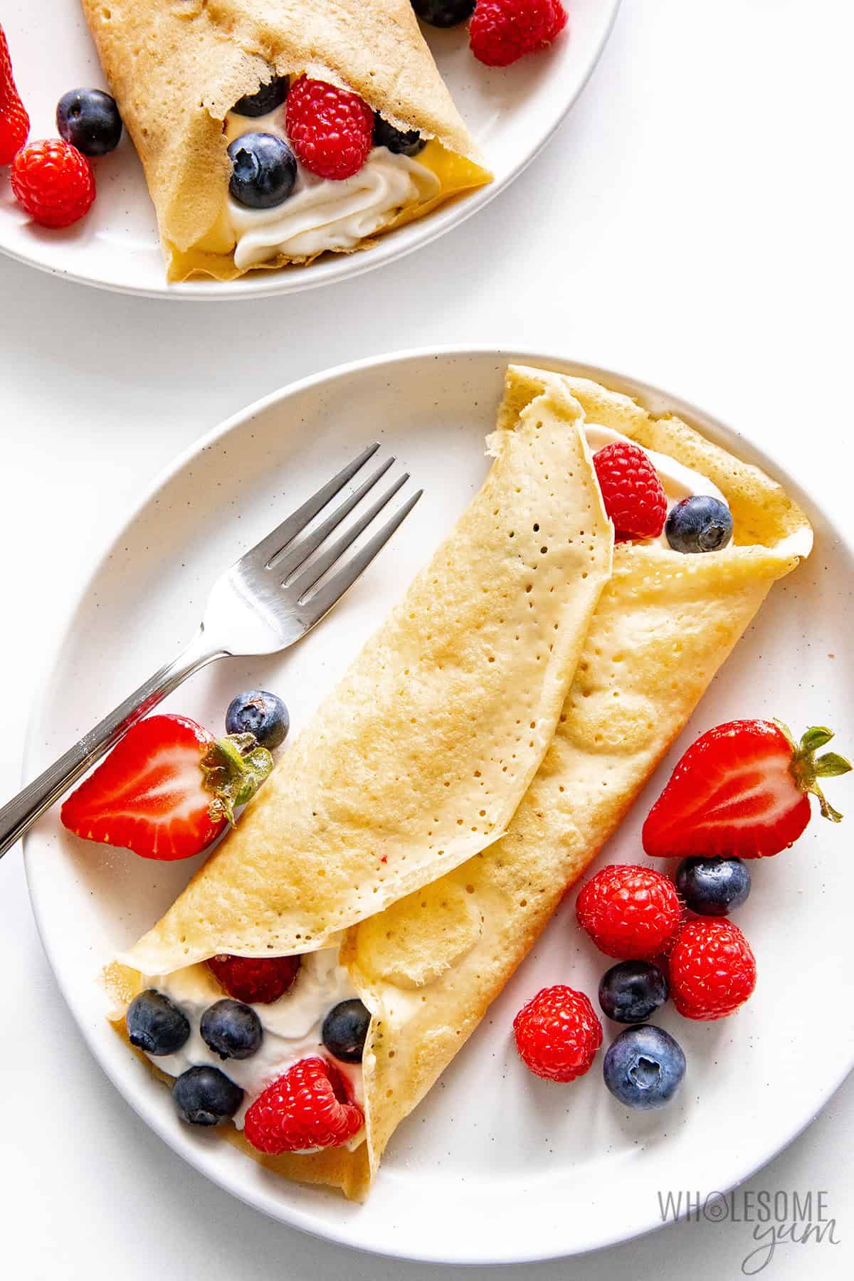 Almond flour crepes filled with berries and whipped cream on 2 plates.