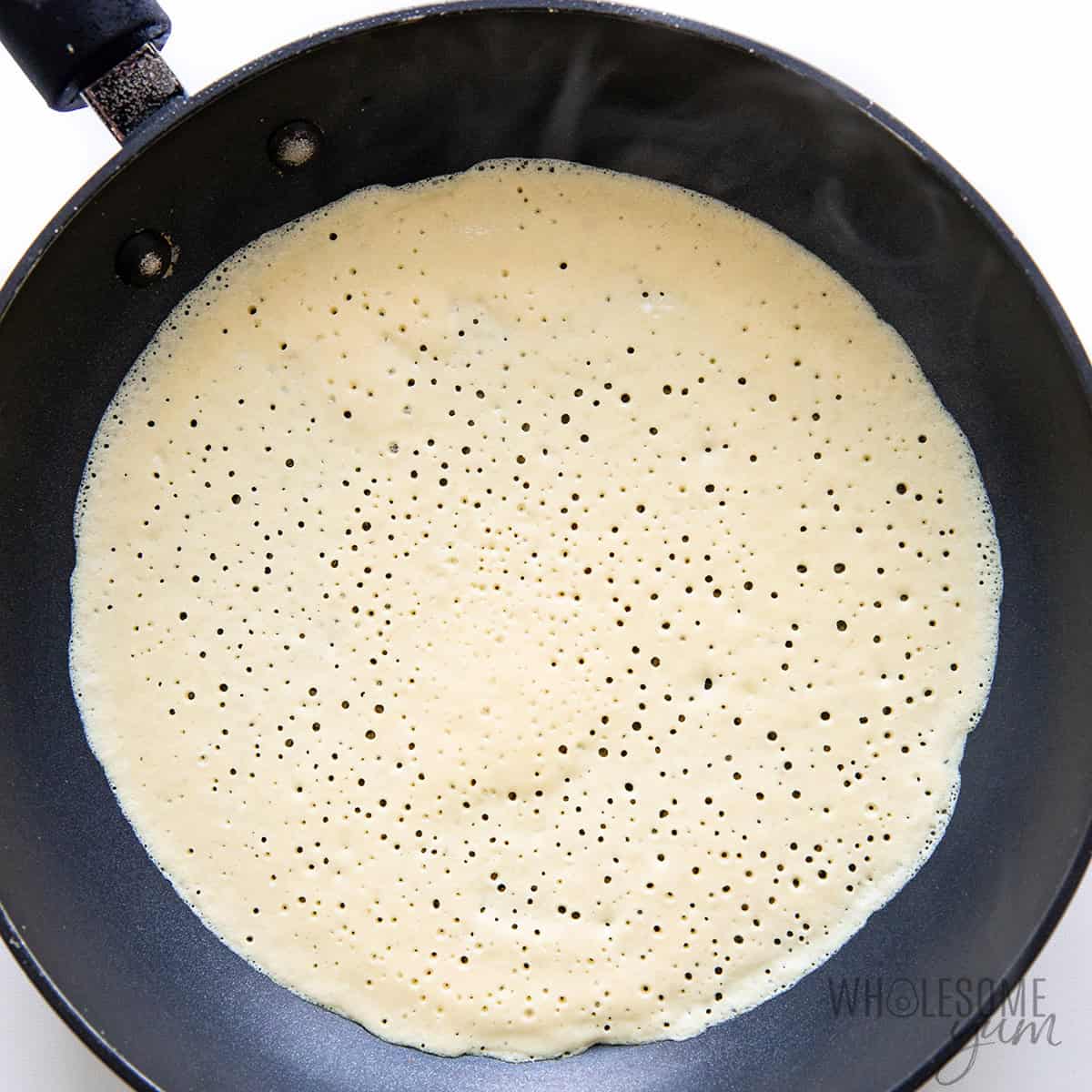 Thin layer of batter in a skillet with bubbles forming, indicating it's time to flip.