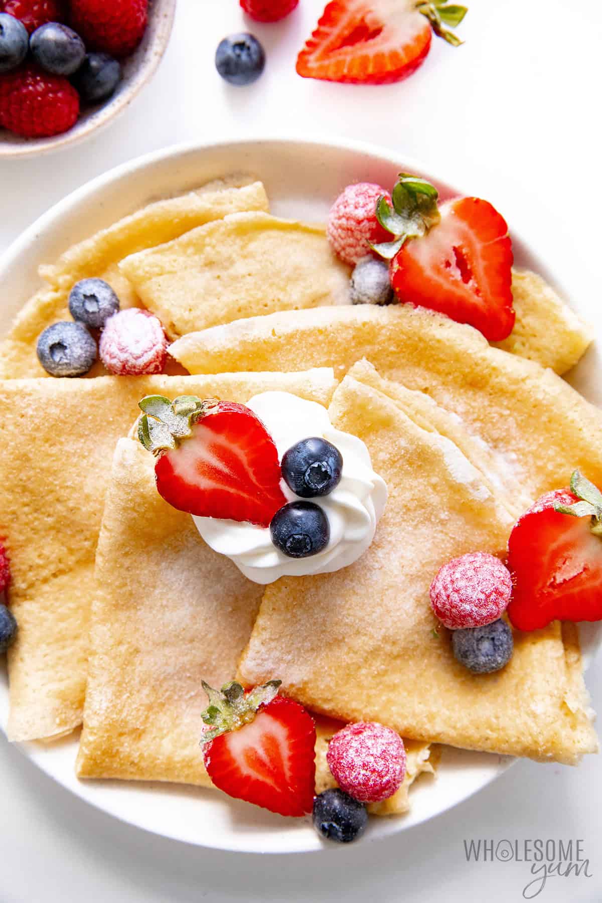 Soft, flexible almond flour crepes on a plate with berries and powdered Besti.