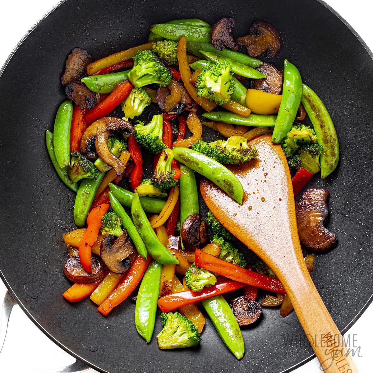 Vegetables in a wok stirred with a wooden spoon. 