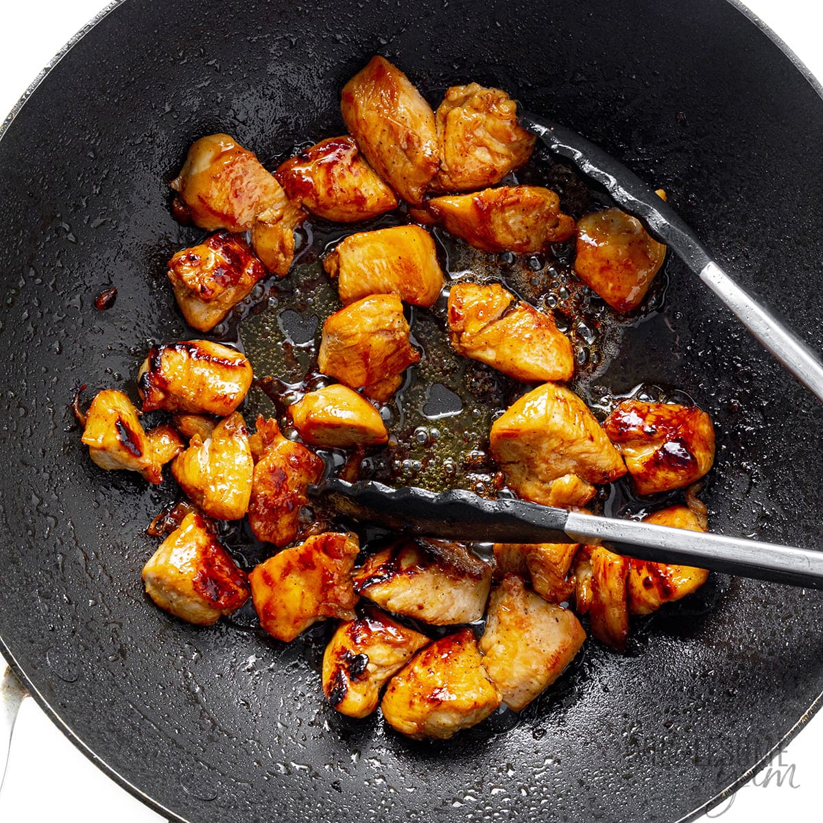 Stir fried chicken in a wok with tongs.