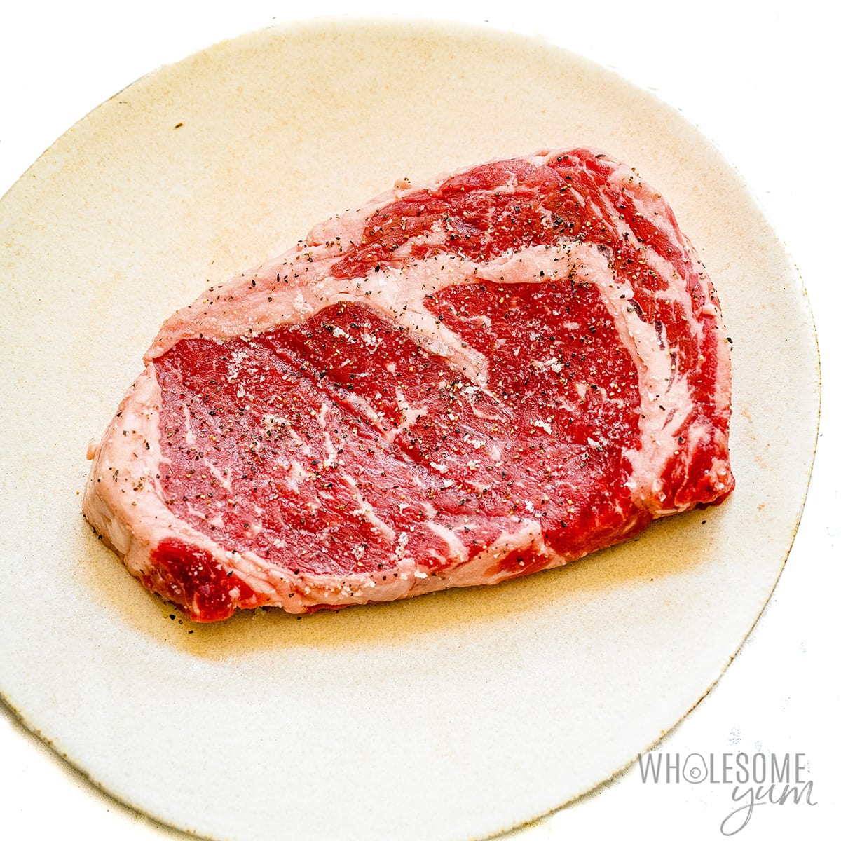 Raw seasoned steak on a plate.