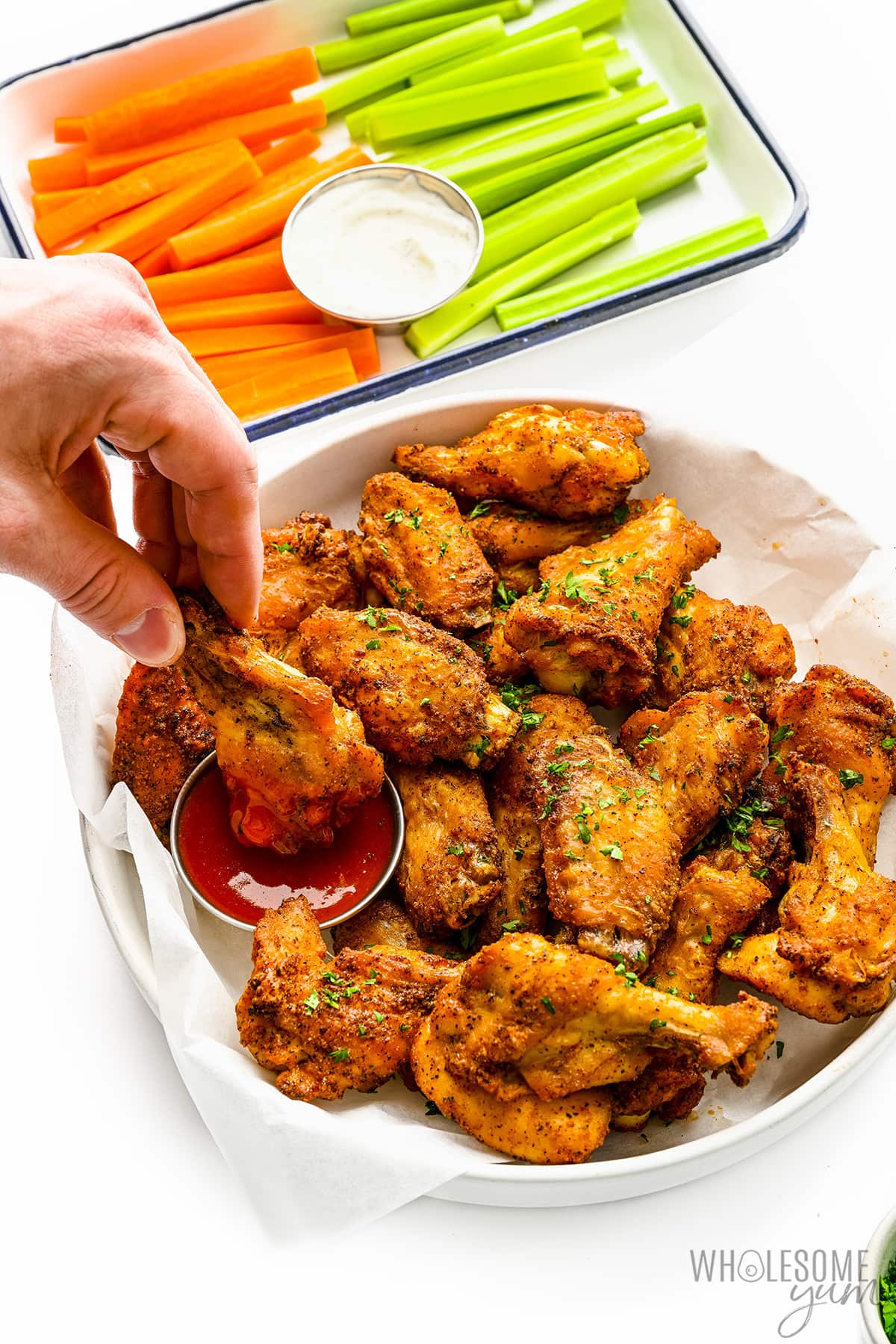 Crispy baked chicken wings dipped into sauce, next to platter of celery and carrots.