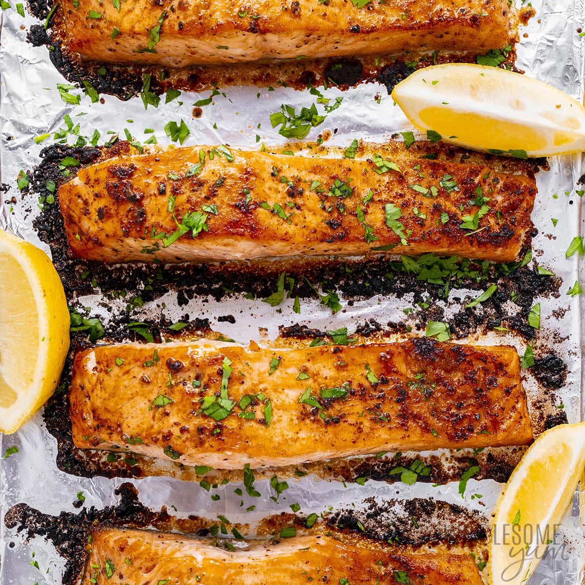 Broiled salmon on baking sheet with lemon wedges.