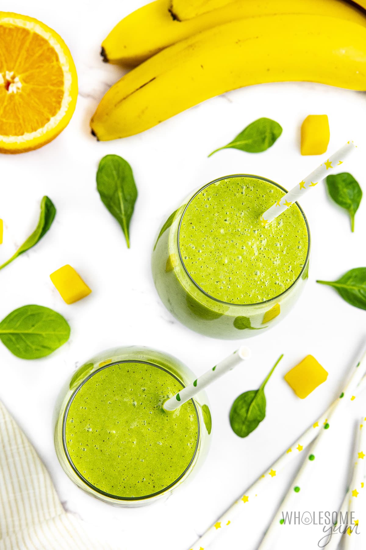 Two spinach smoothies with bananas and a slice of orange on the side.
