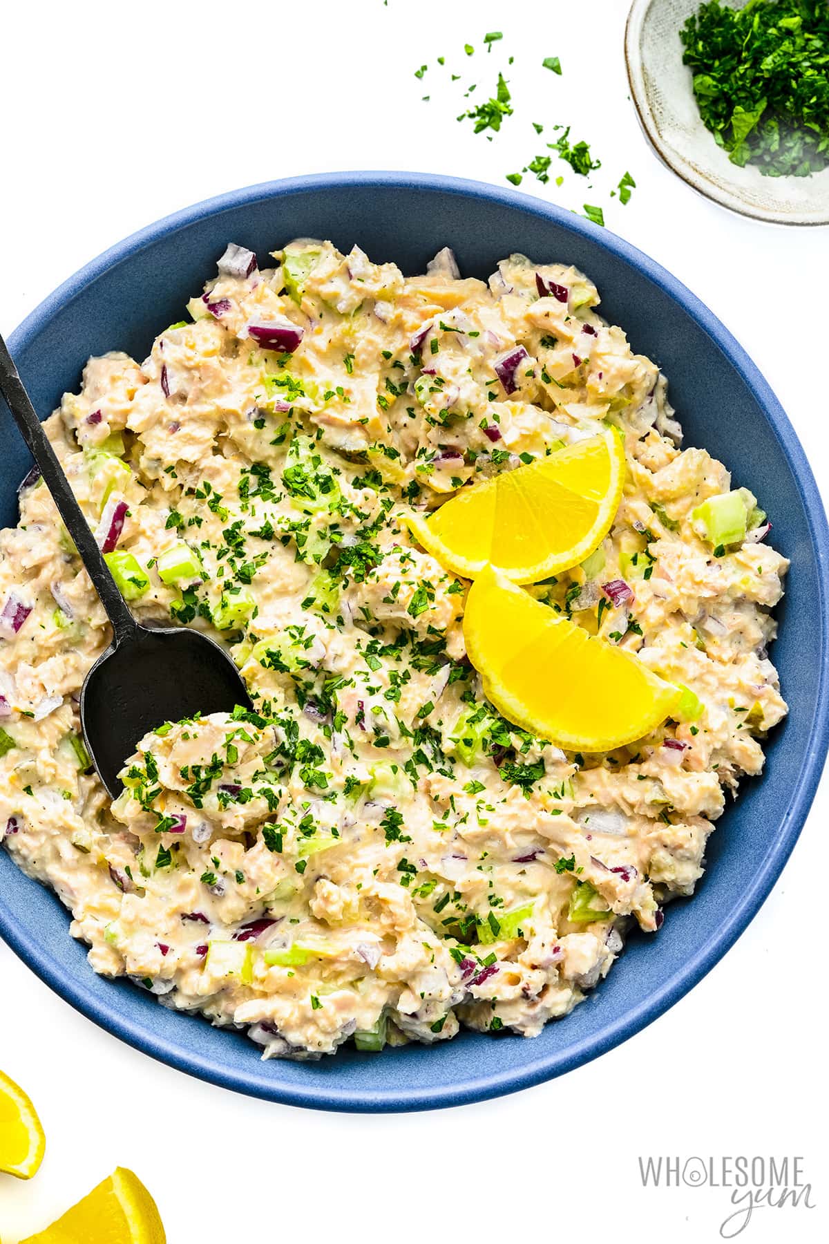 Tuna salad in a bowl with lemon slices and a spoon.