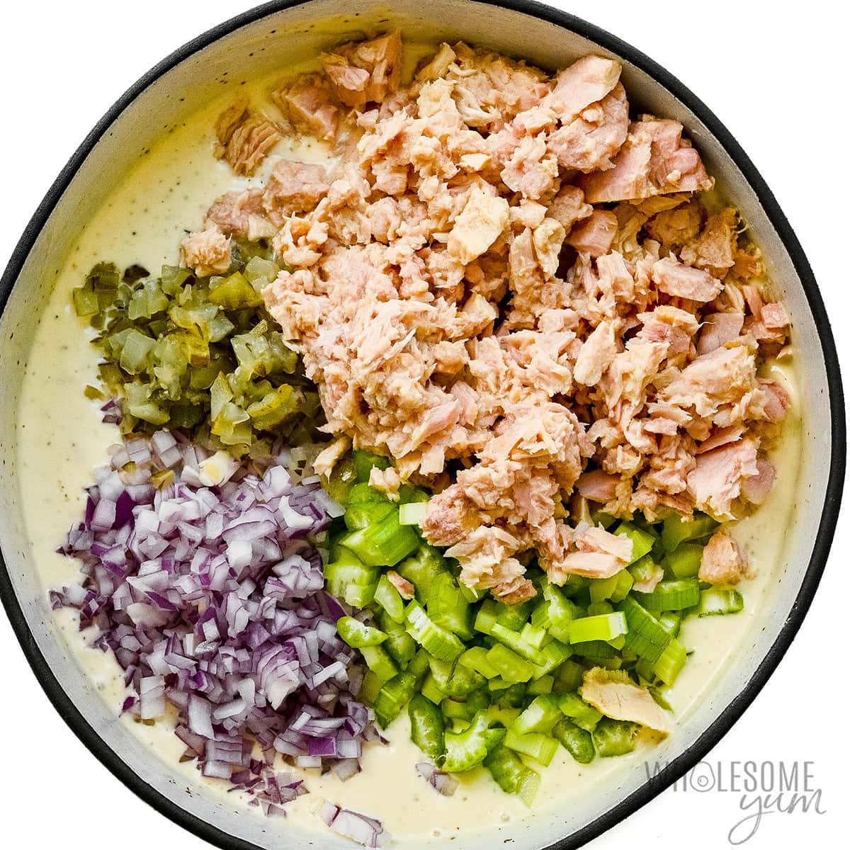 Tuna, celery, onion, pickles, and parsley in the bowl with dressing.