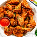 Oven baked chicken wings on a plate with dipping sauce.
