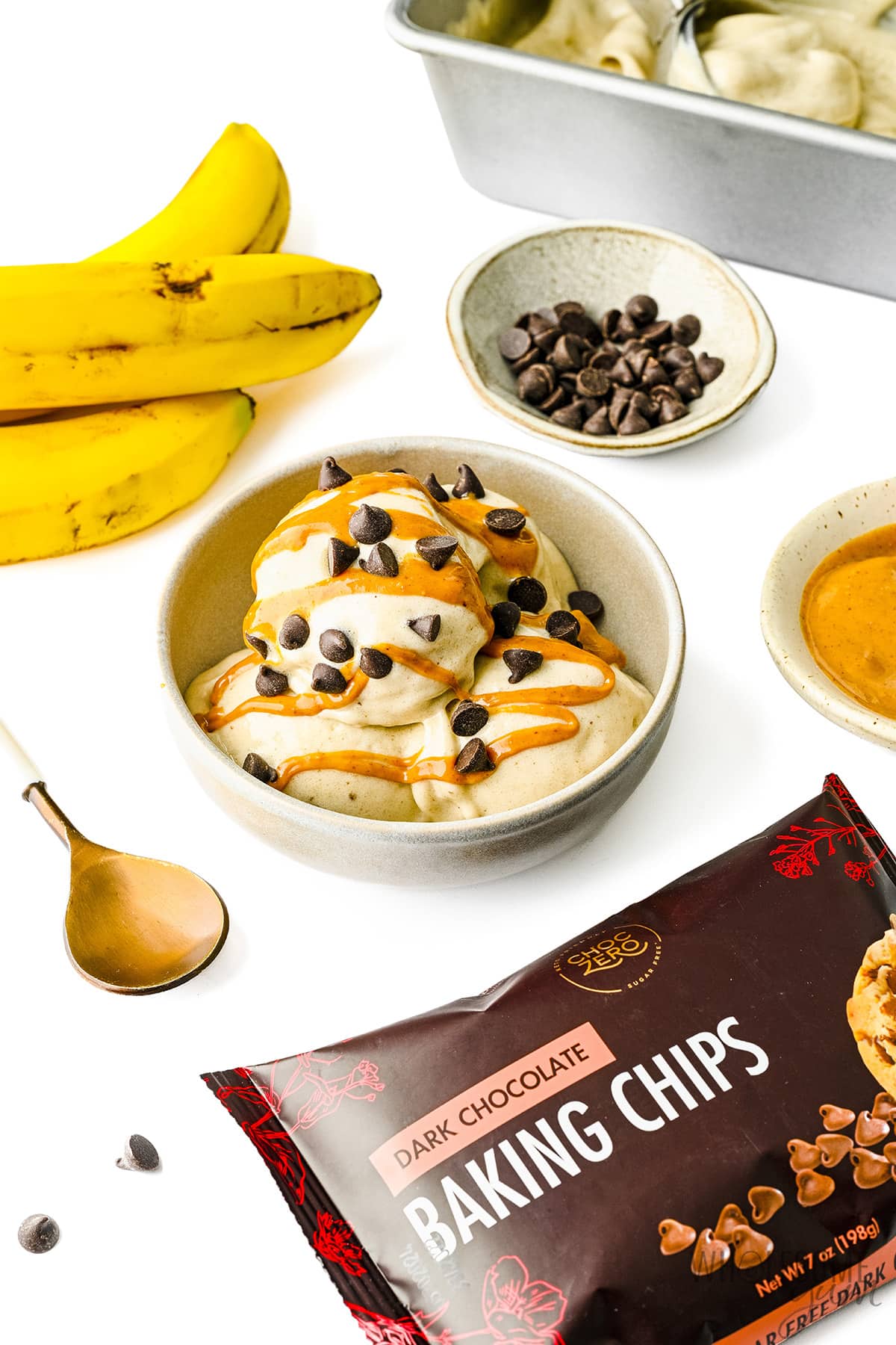 Banana ice cream in a bowl next to chocolate chips and bananas.