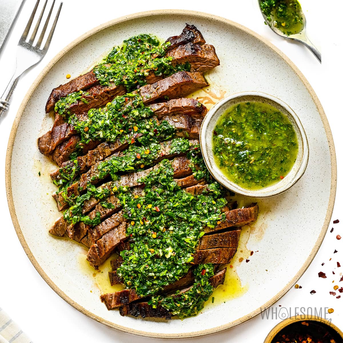 Sliced flank steak with chimichurri sauce on a plate.