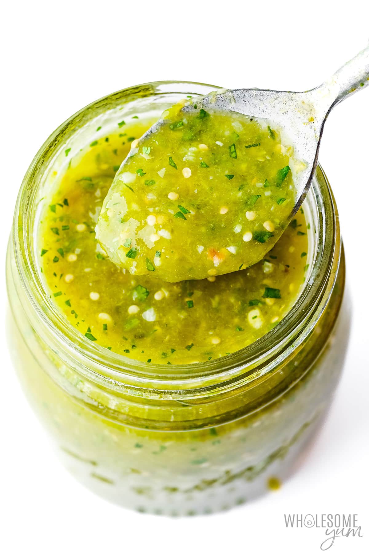 Salsa verde in a mason jar with a spoonful scooped out.