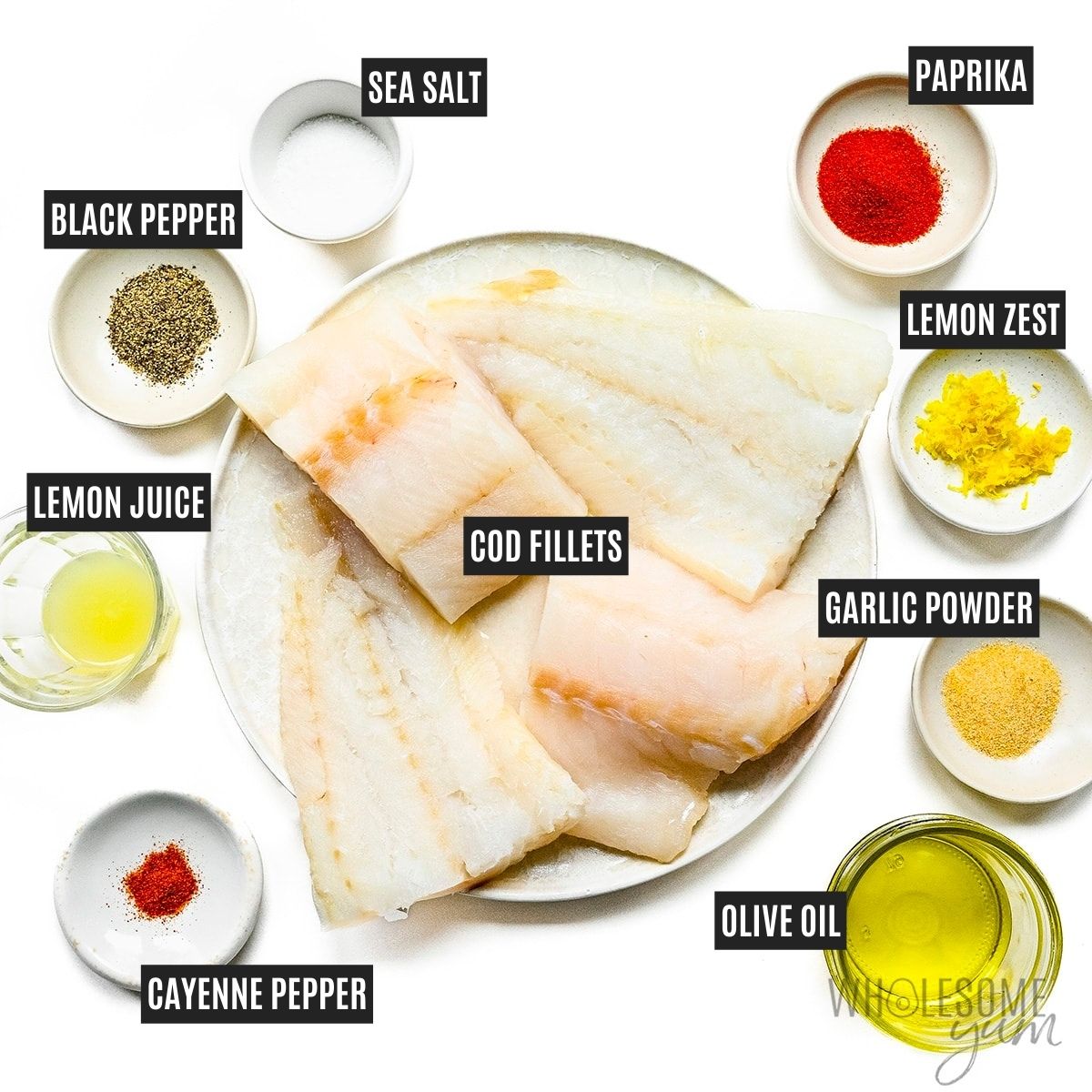 Cod fillets on a plate next to lemon juice and zest, olive oil, and spices in small bowls with labels.