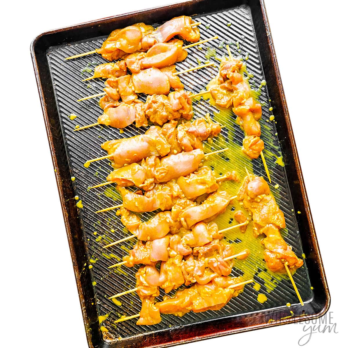 Marinated chicken placed on skewers on a baking sheet.