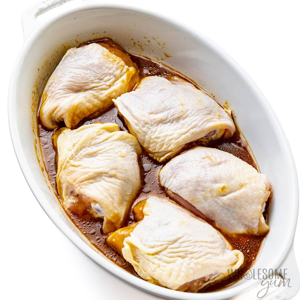 Bone-in chicken thighs in baking dish with marinade.