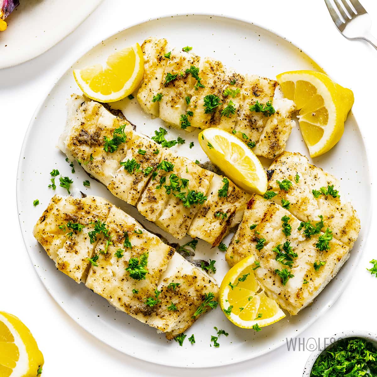 Grilled halibut recipe on a plate with lemon wedges.