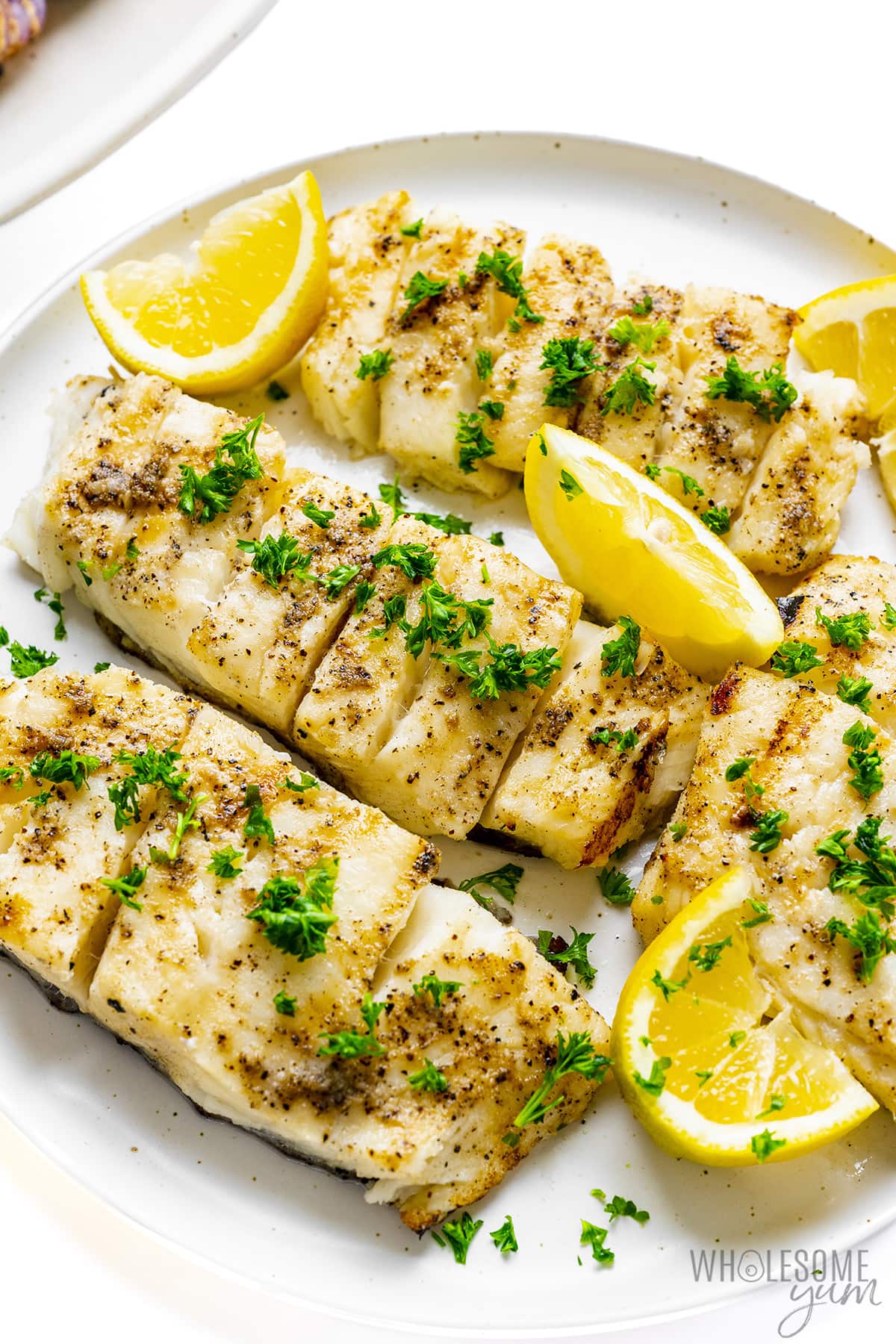Grilled halibut on a plate with lemon wedges.