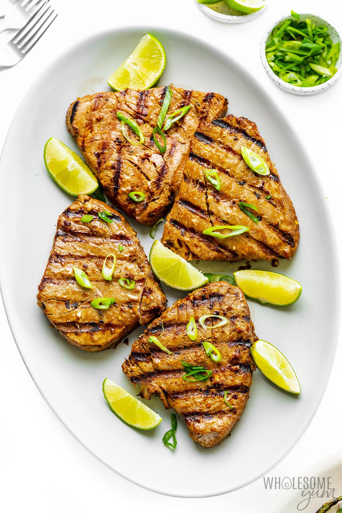 Grilled tuna steaks on a platter with green onions and lime wedges.