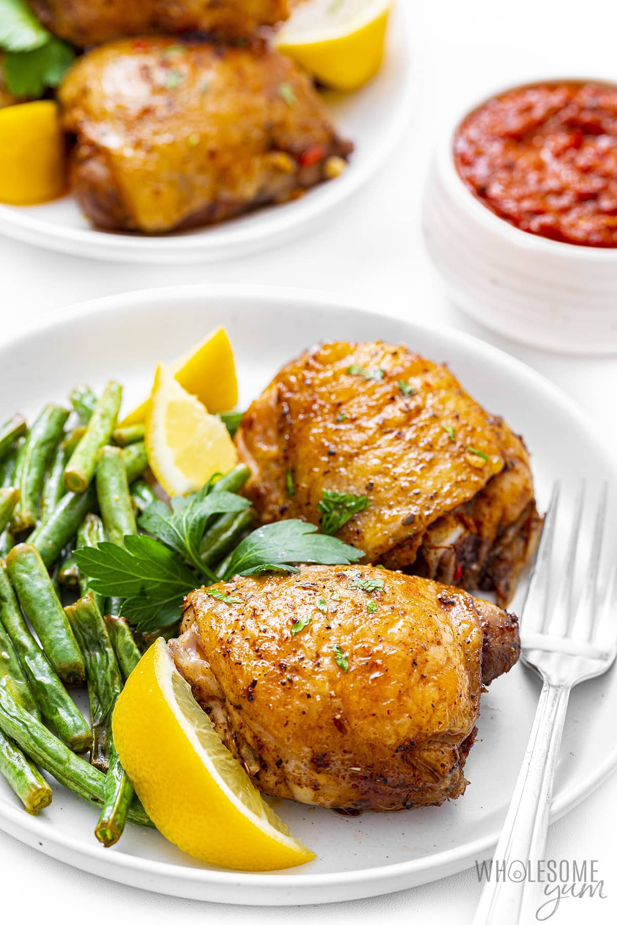 Peri peri chicken recipe on a plate with sauce, green beans, and lemon wedges.