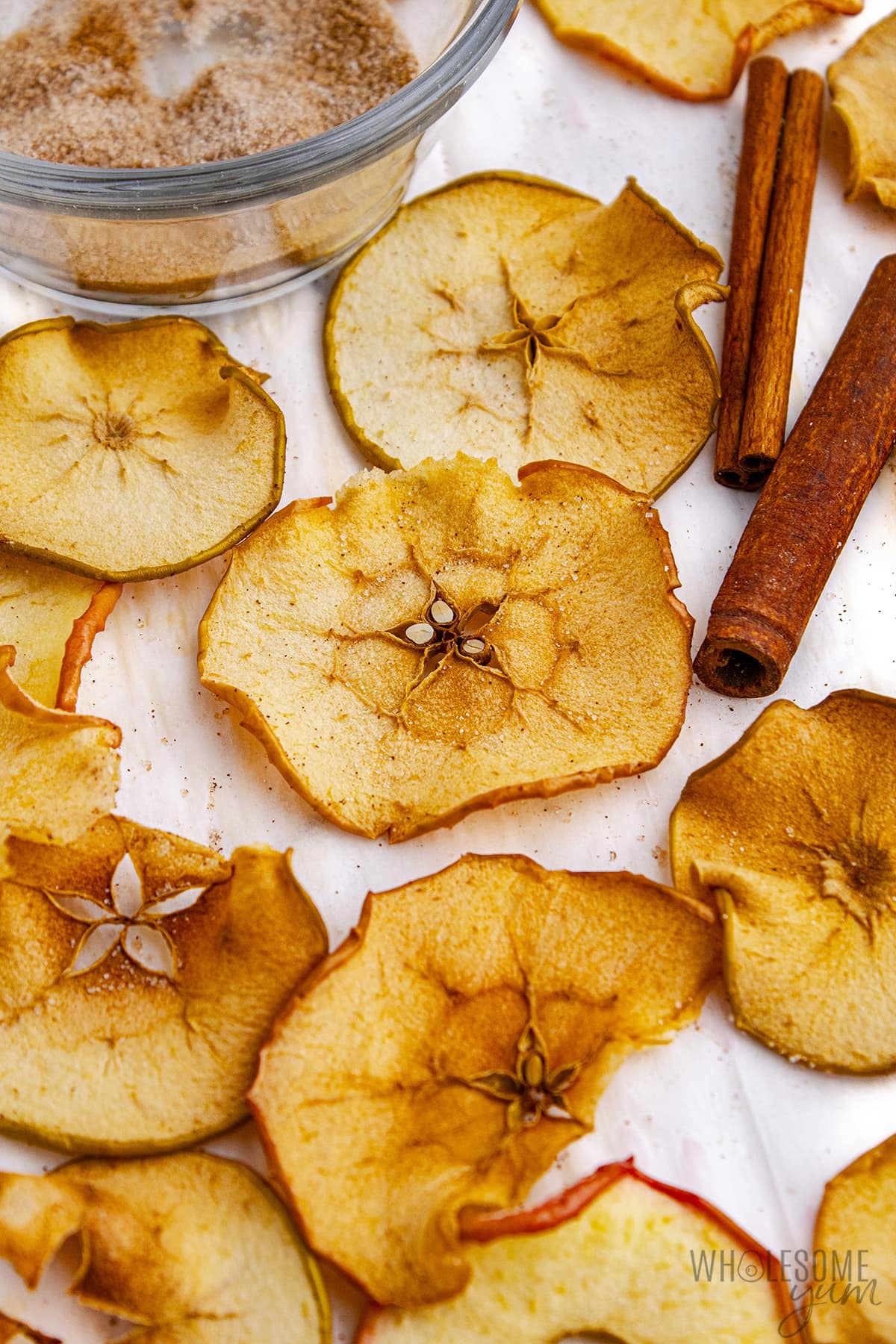 Apple chips recipe on parchment next to cinnamon sticks.