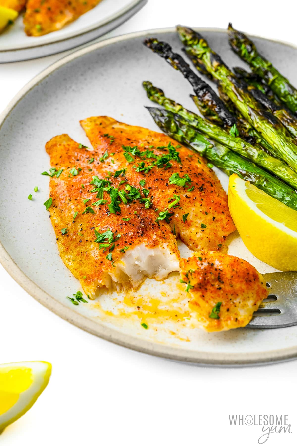 Baked flounder recipe flaked with a fork, plated with asparagus.
