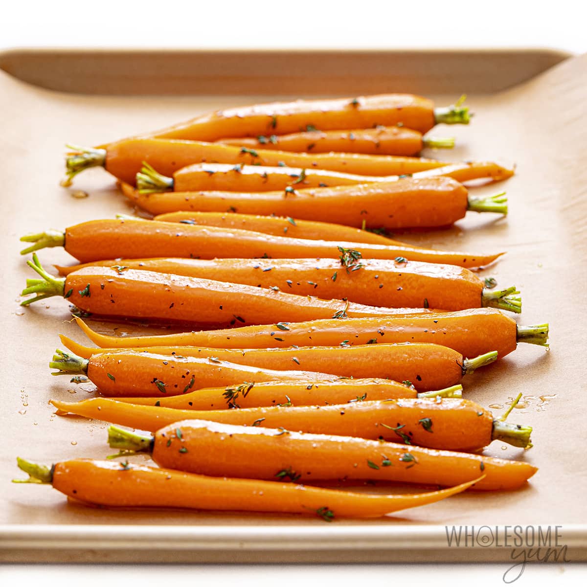 Raw carrots with honey mixture on lined baking sheet.
