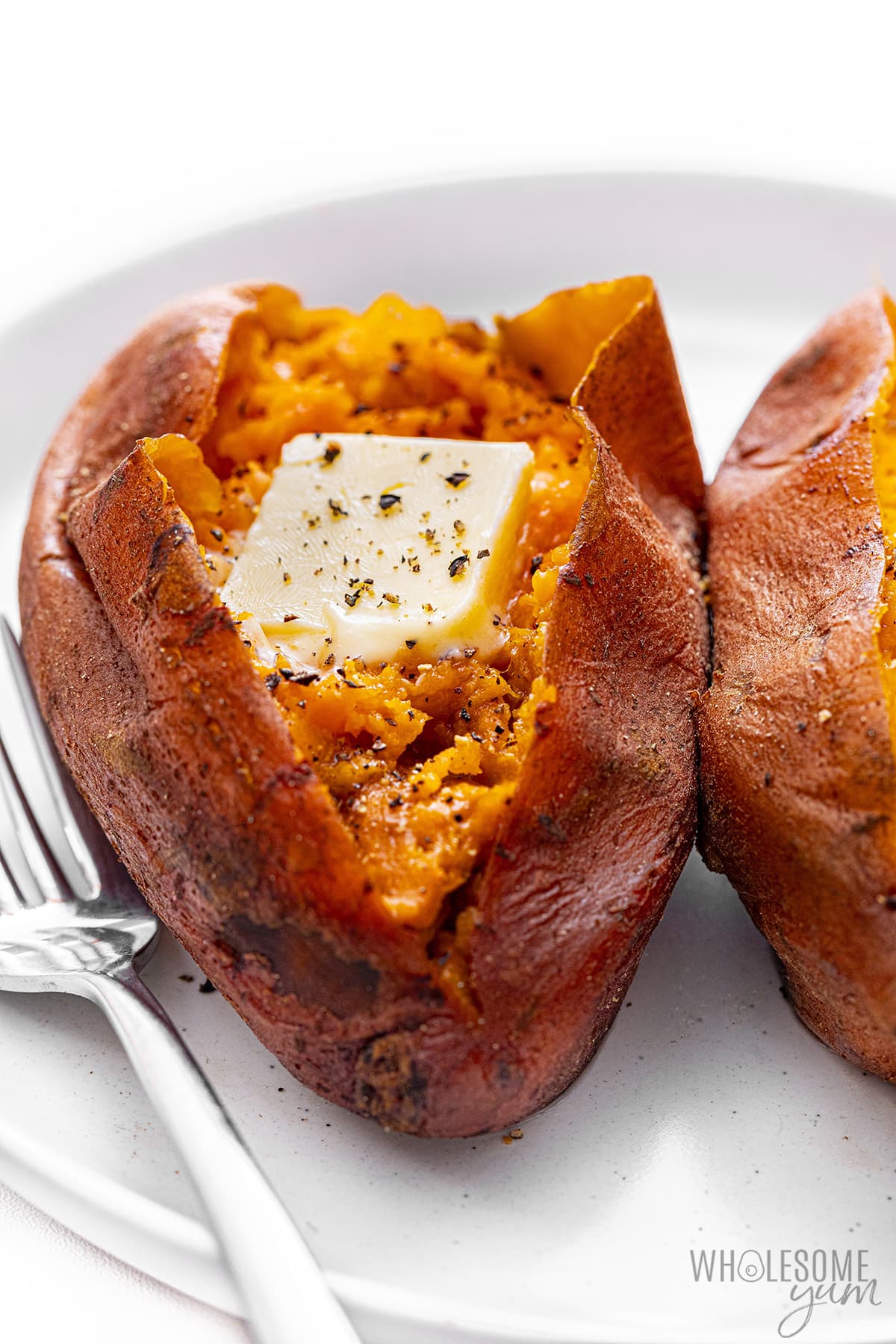 Instant Pot Sweet Potatoes, served with a fork on a plate and basted with butter.