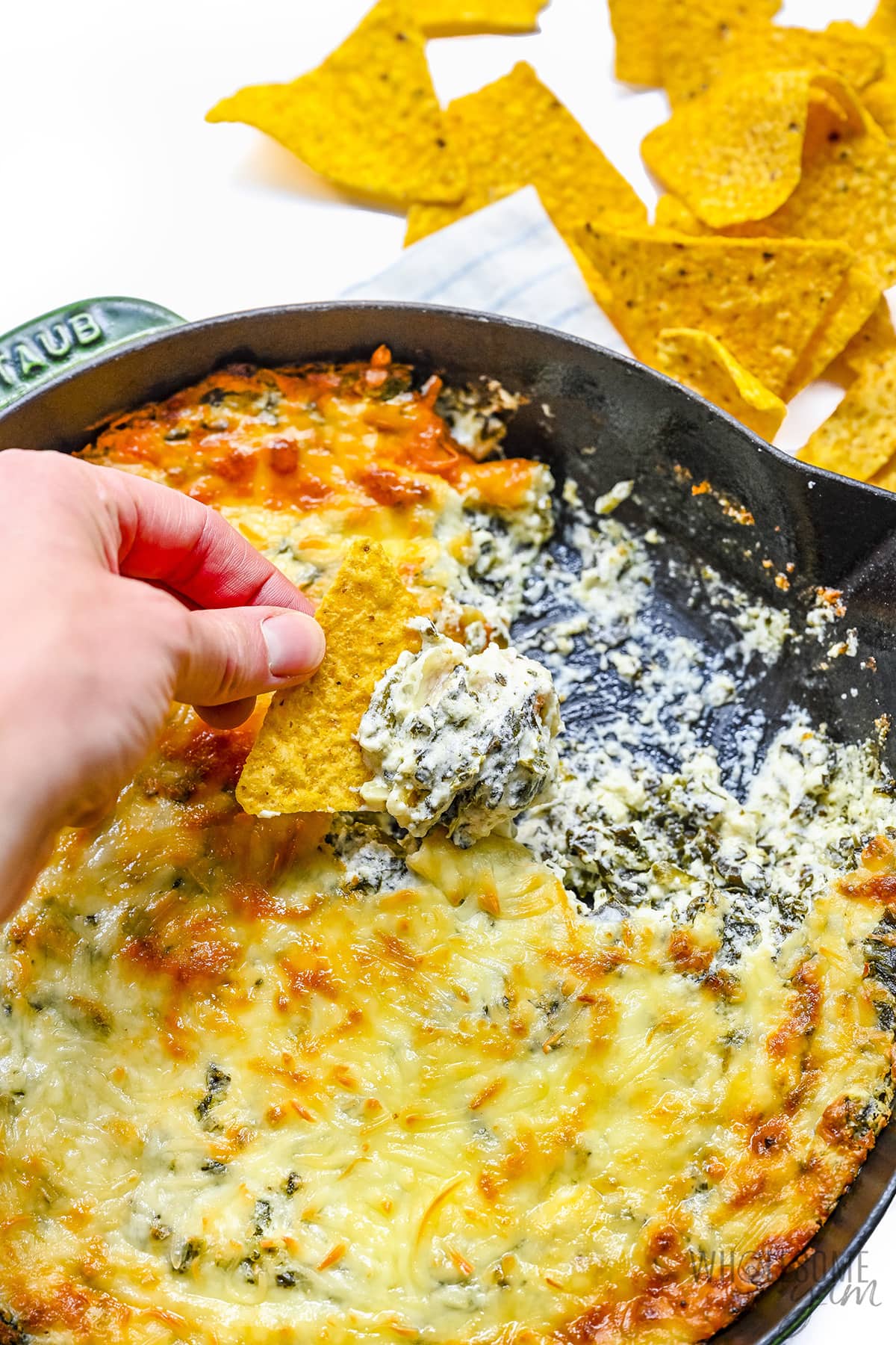 Scooping spinach dip with tortilla chips.