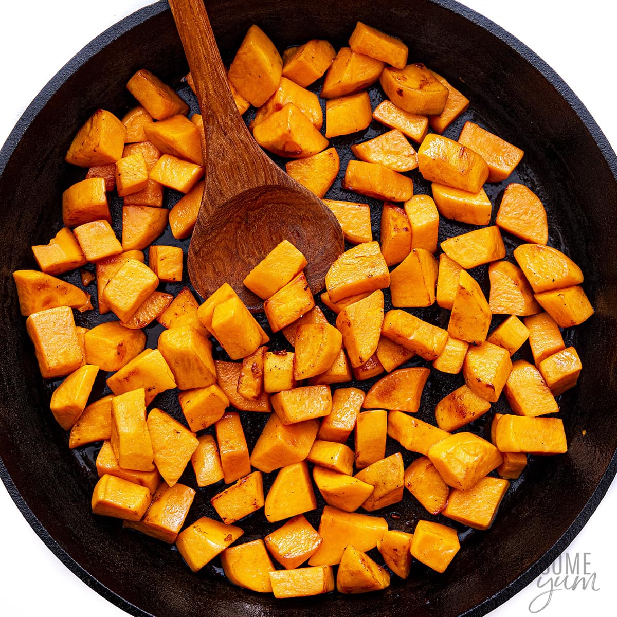 Sweet potatoes in a skillet with a wooden spoon.