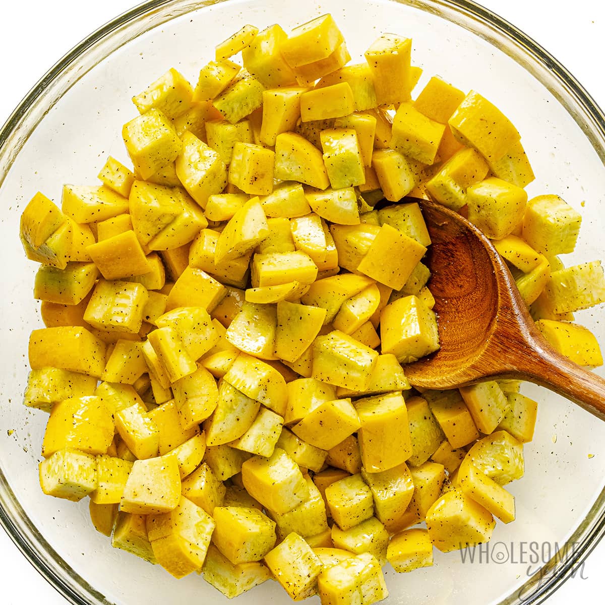 Seasoned squash cubes in a bowl with a wooden spoon.