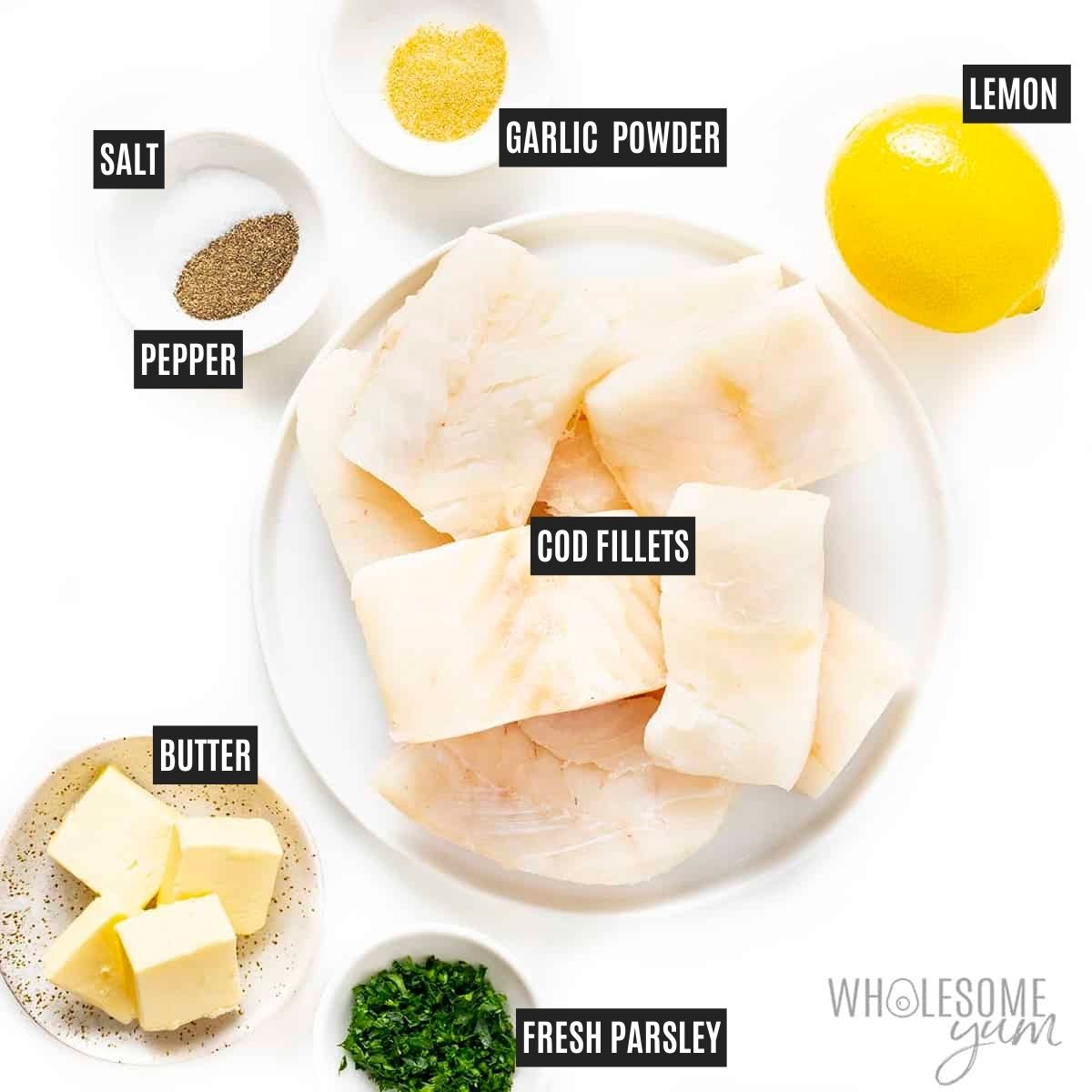 Cod fish fillets on a plate next to small labeled bowls of butter, lemon, parsley, garlic powder, salt, and pepper.