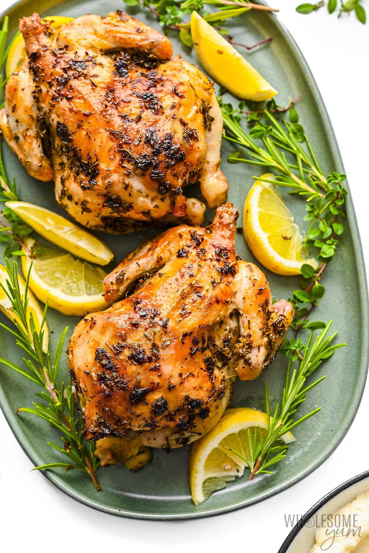 Cornish hen is served on a plate with lemon wedges and fresh herbs.