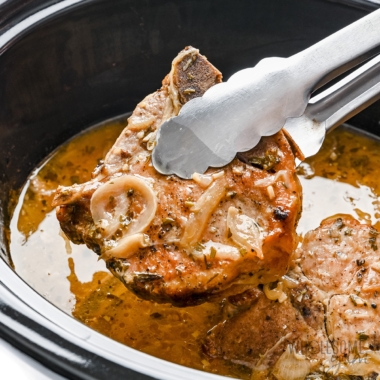 Crock Pot pork chops lifted out of slow cooker with tongs.