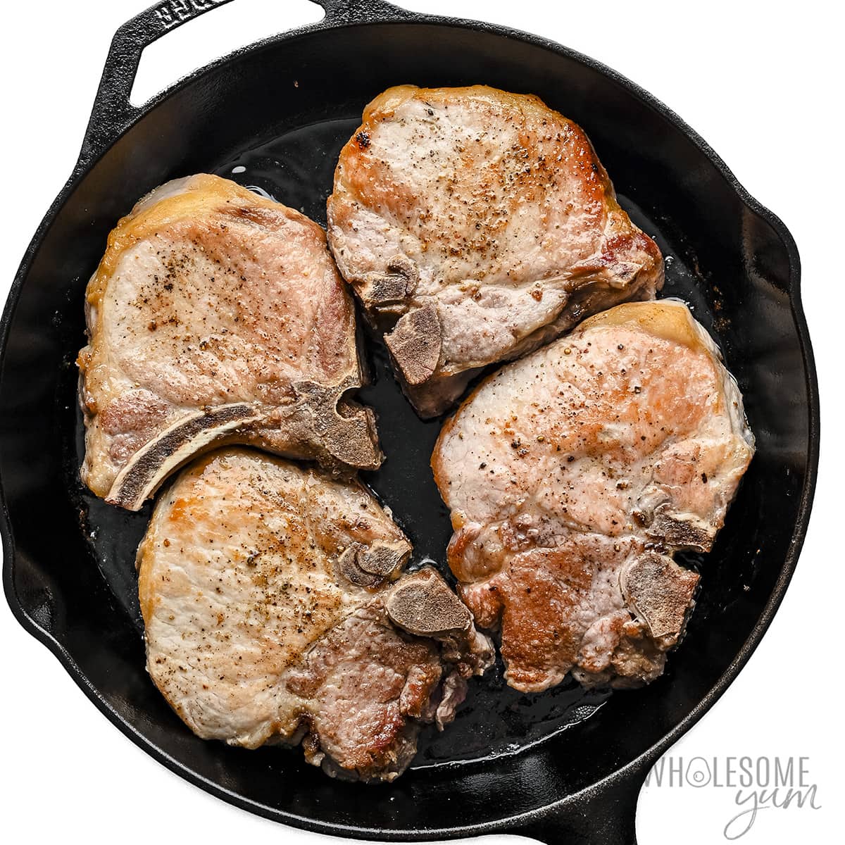 Pork chops seared on both sides in a skillet.