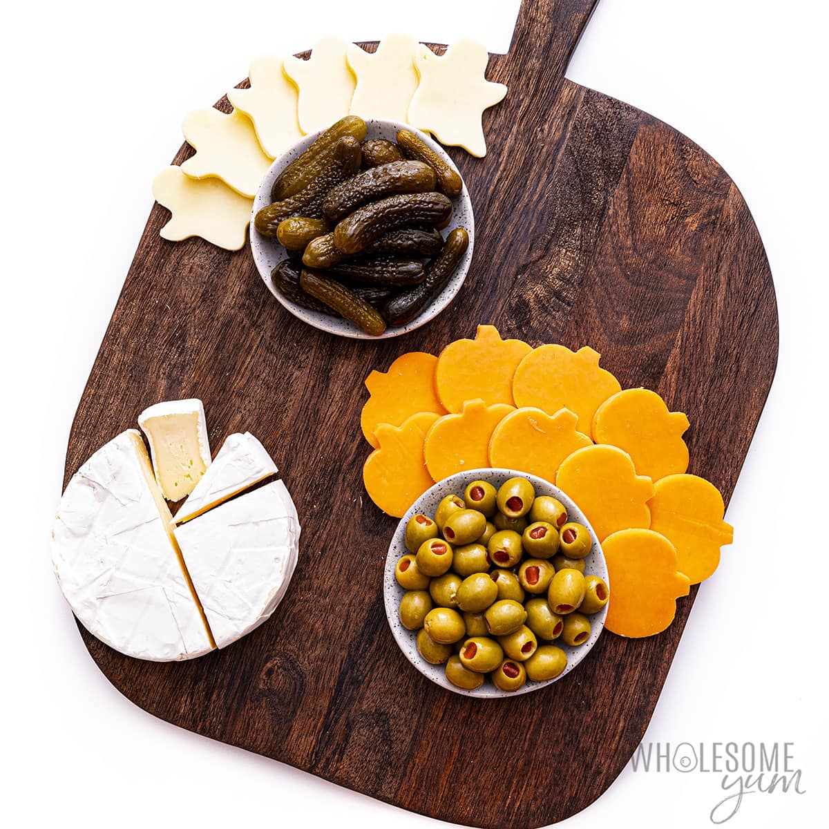 Cheese, olives and pickles are placed on the plate.