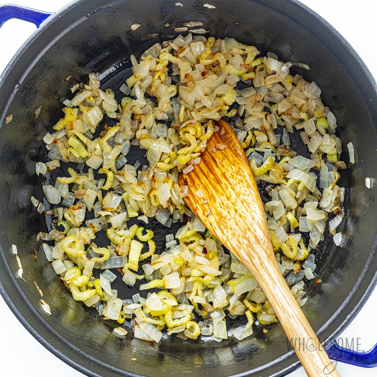 Sauteed onion and celery in a Dutch oven with a wooden spoon.