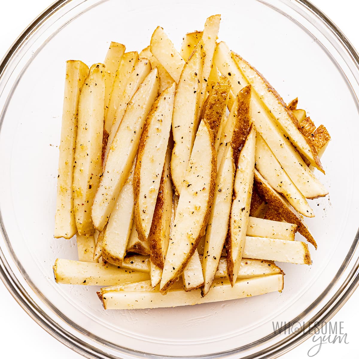 Potato sticks seasoned with garlic powder, salt, and pepper in a bowl.