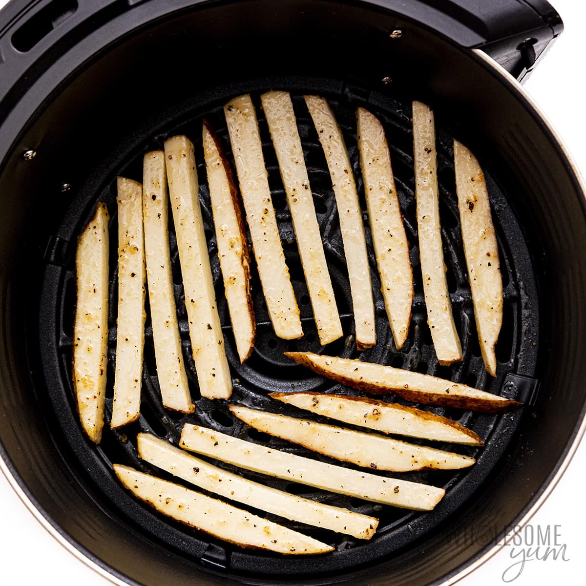 Raw fries in air fryer basket.