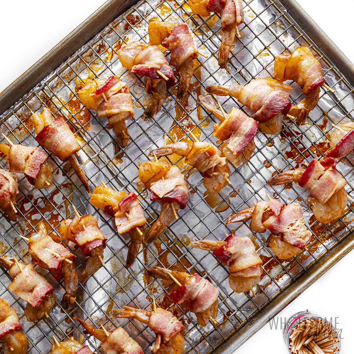 Shrimp wrapped with bacon on a baking sheet with a rack.