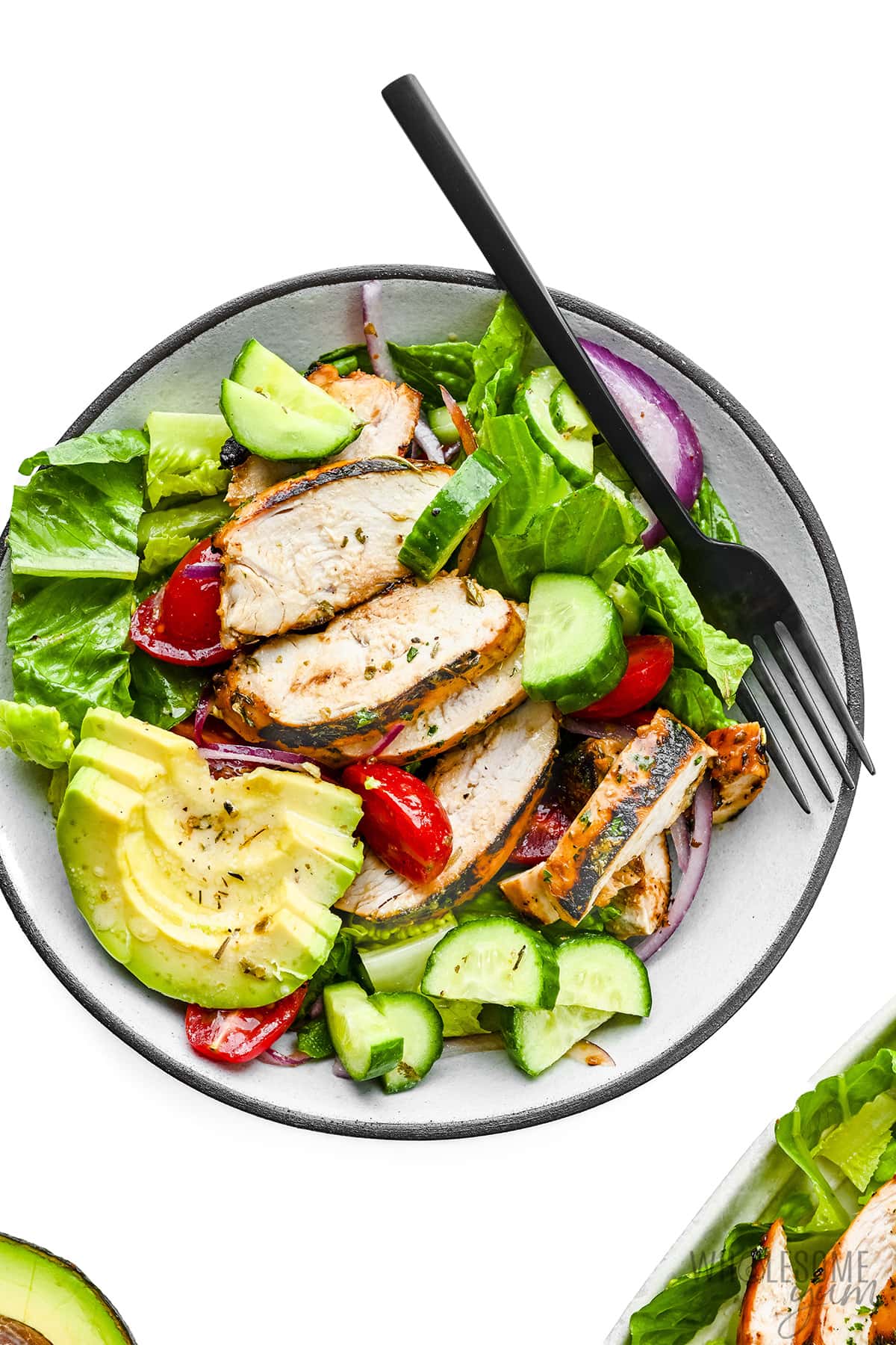 Salad with grilled chicken plated with fork.