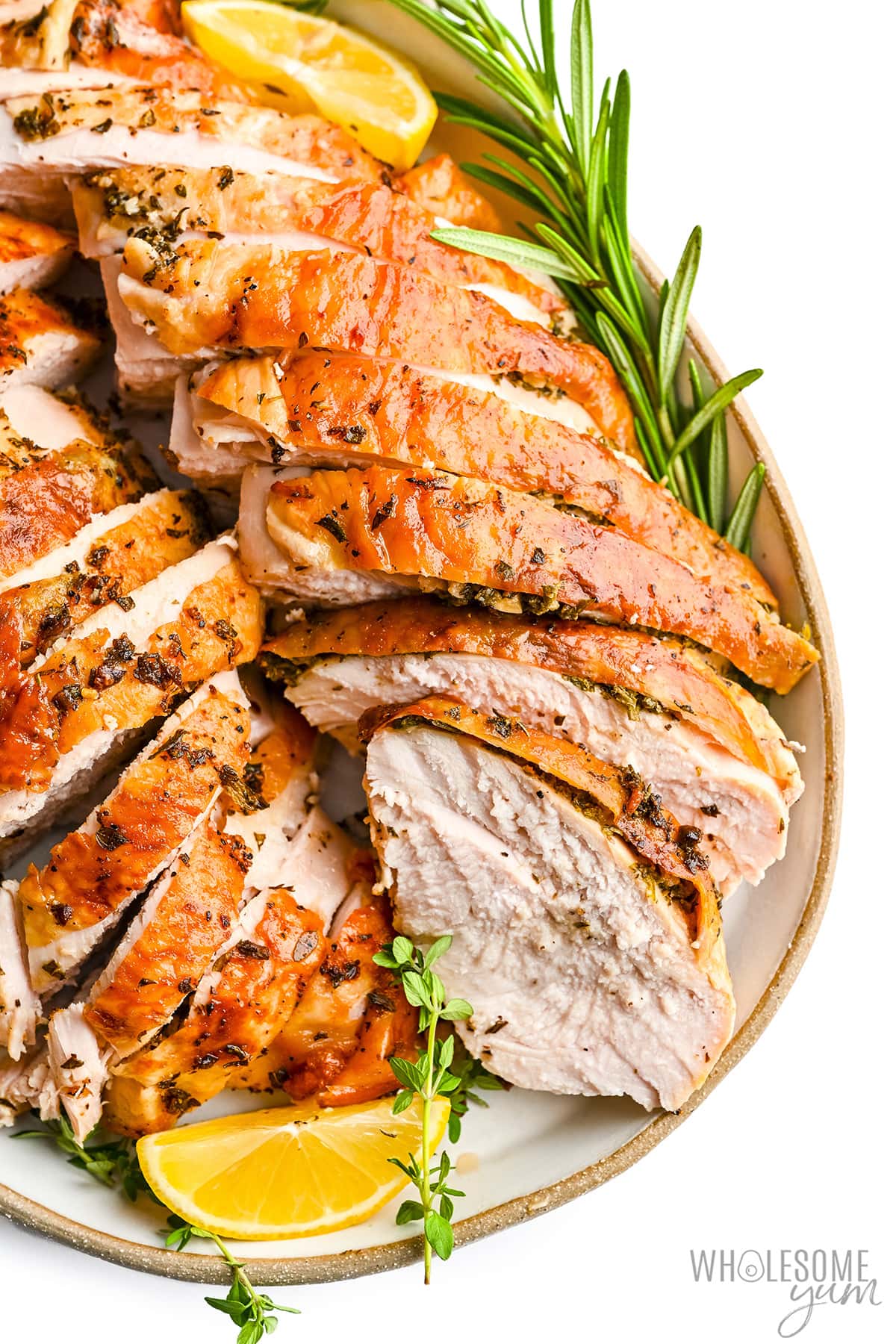 Sliced ​​roasted turkey breast with rosemary sprigs and lemon wedges.