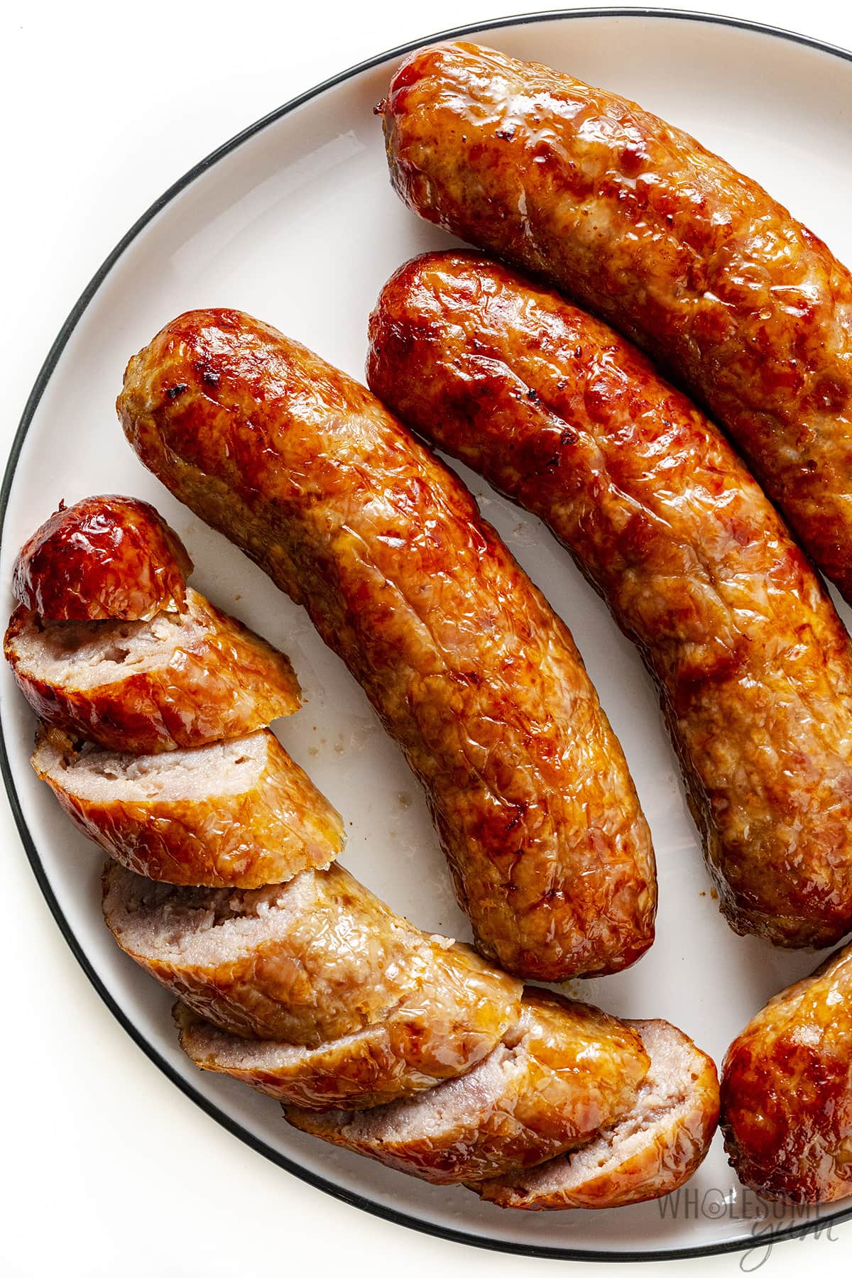 Brats on a plate with one cut into slices.