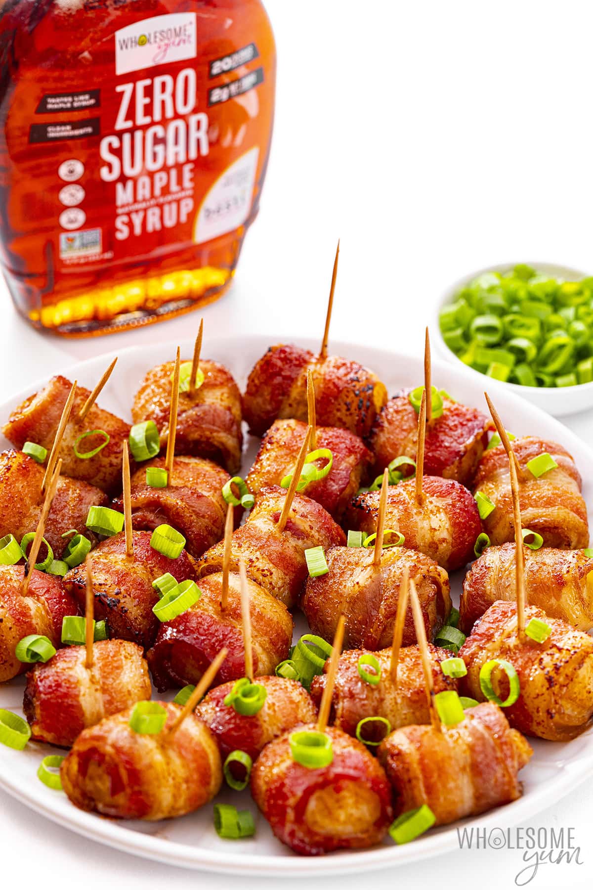 Bacon wrapped water chestnuts on a plate next to maple syrup.
