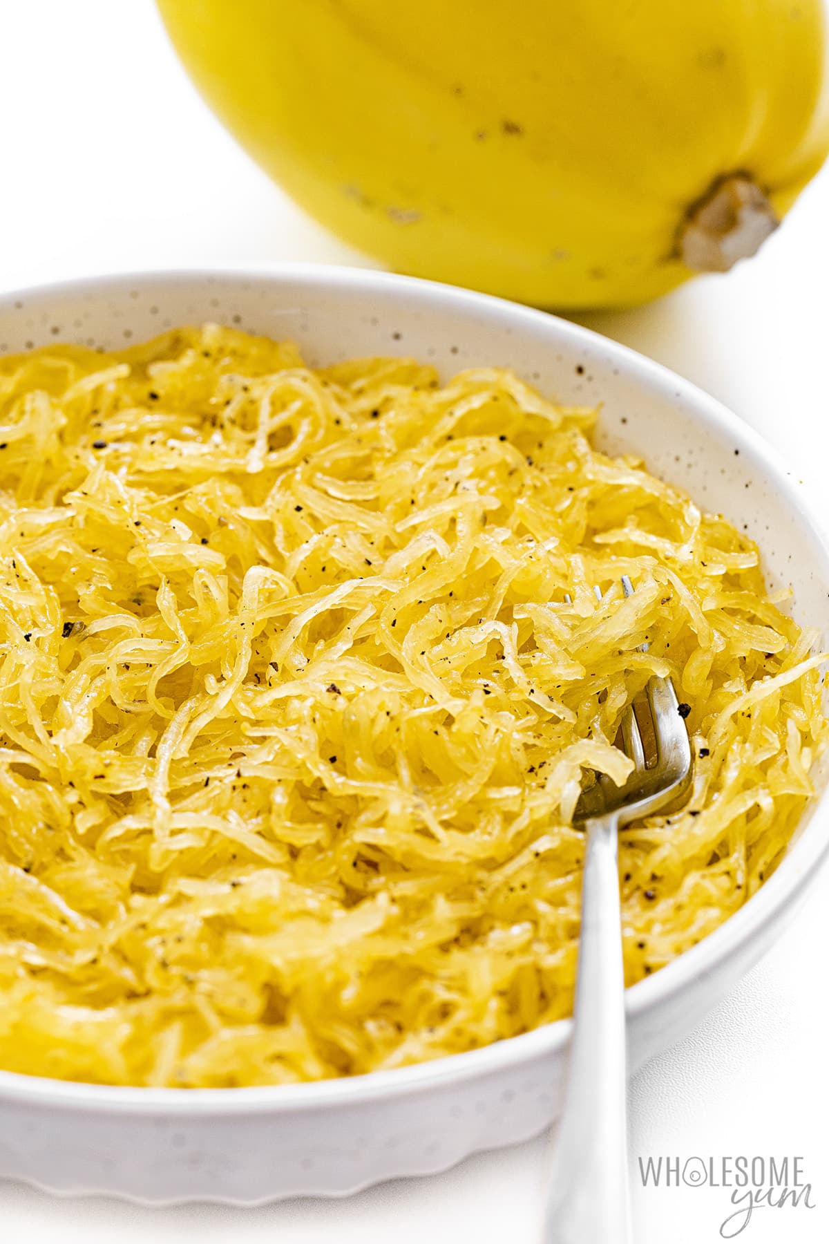 Microwave spaghetti squash in a bowl with pumpkin in the background.