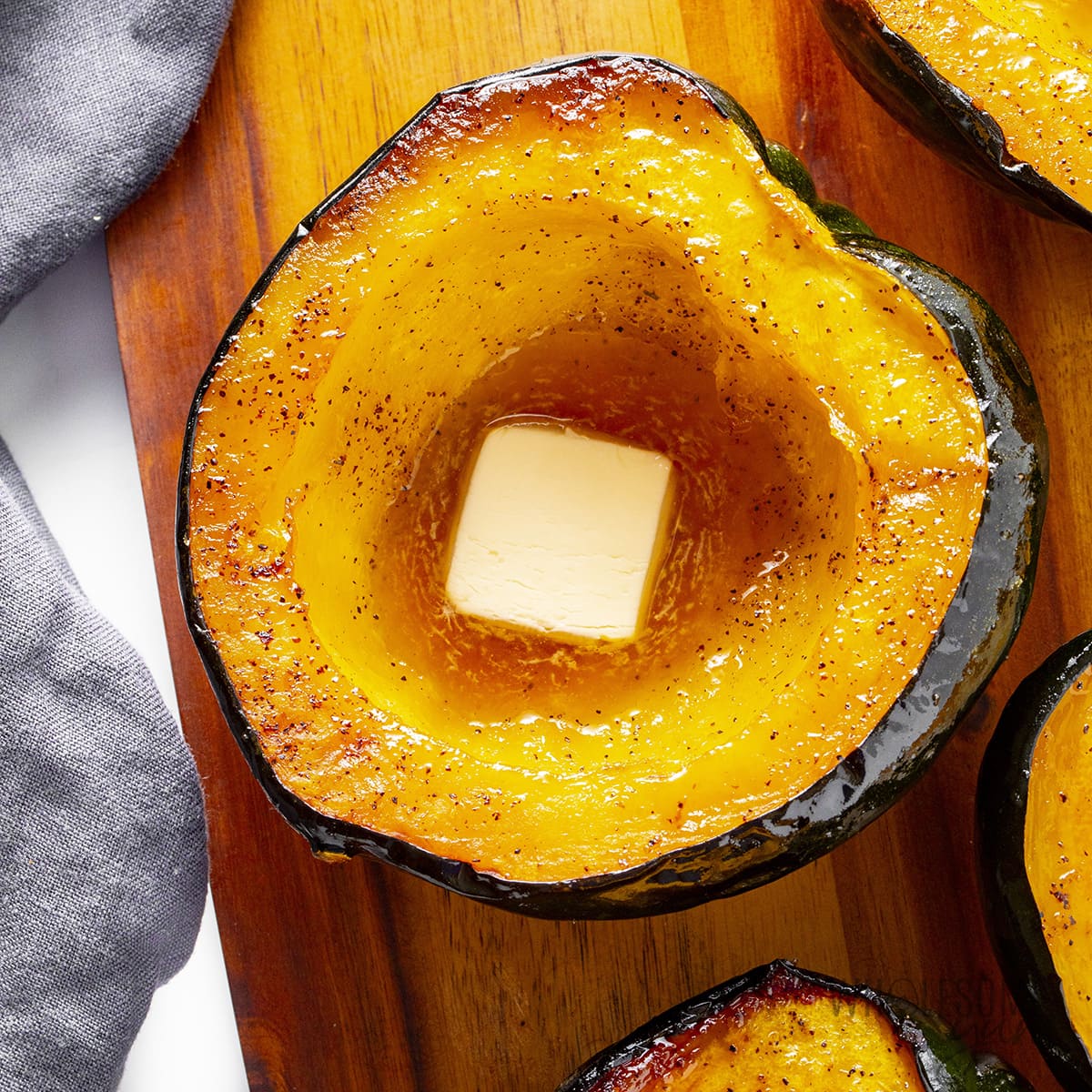 Roasted acorn squash topped with butter on a cutting board.