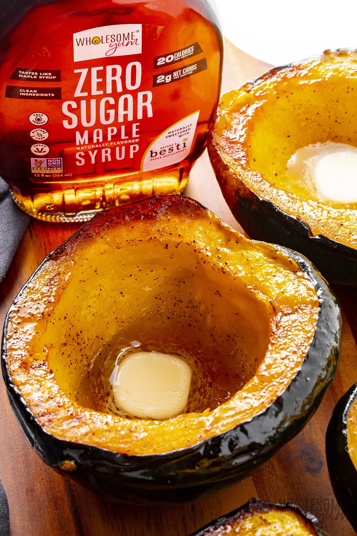Roasted acorn squash on a cutting board next to maple syrup.